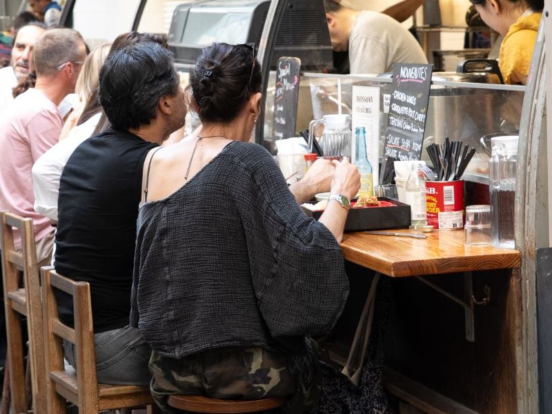 Bezoekers lunchen aan gedeelde tafels op de binnenplaats van Marché des Enfants Rouges